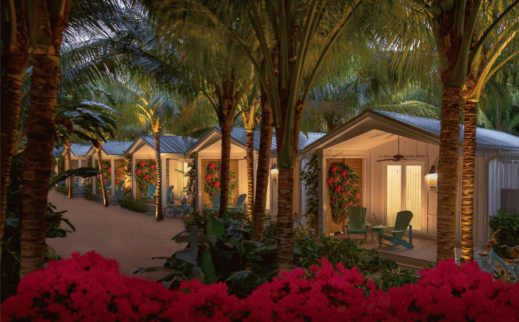 exterior image of bungalows at night with palm trees and flowers