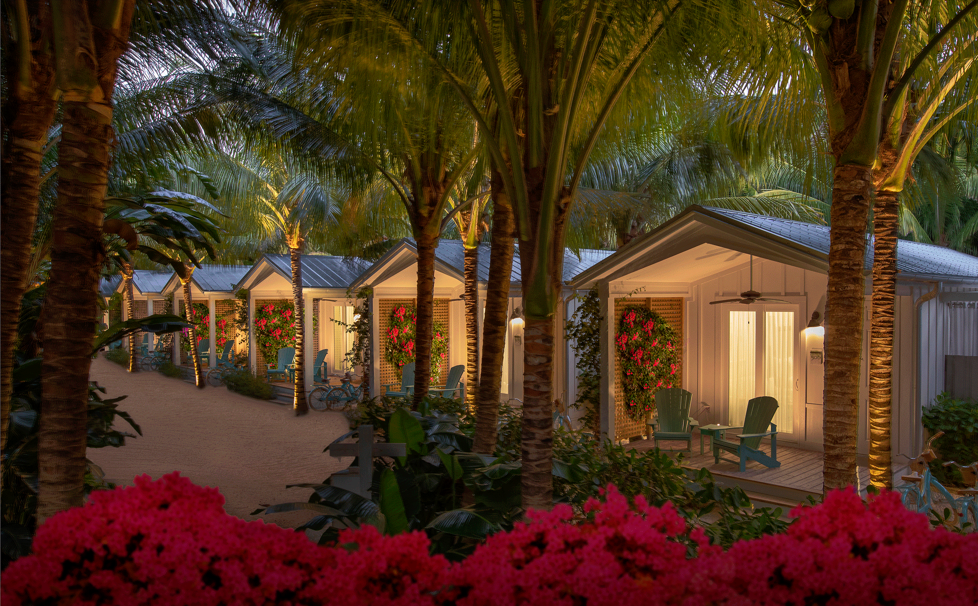 exterior image of bungalows at night with palm trees and flowers