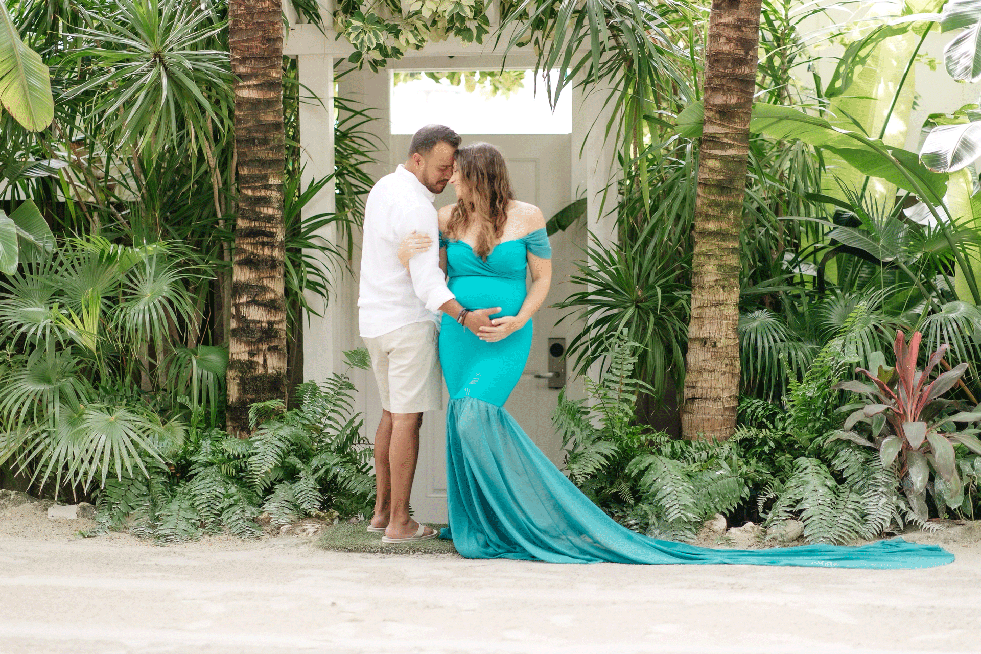 a couple posing outside of their bungalow on the beach during their babymoon