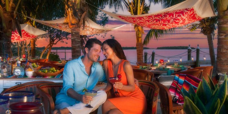 couple sitting by water enjoying margaritas at sunset