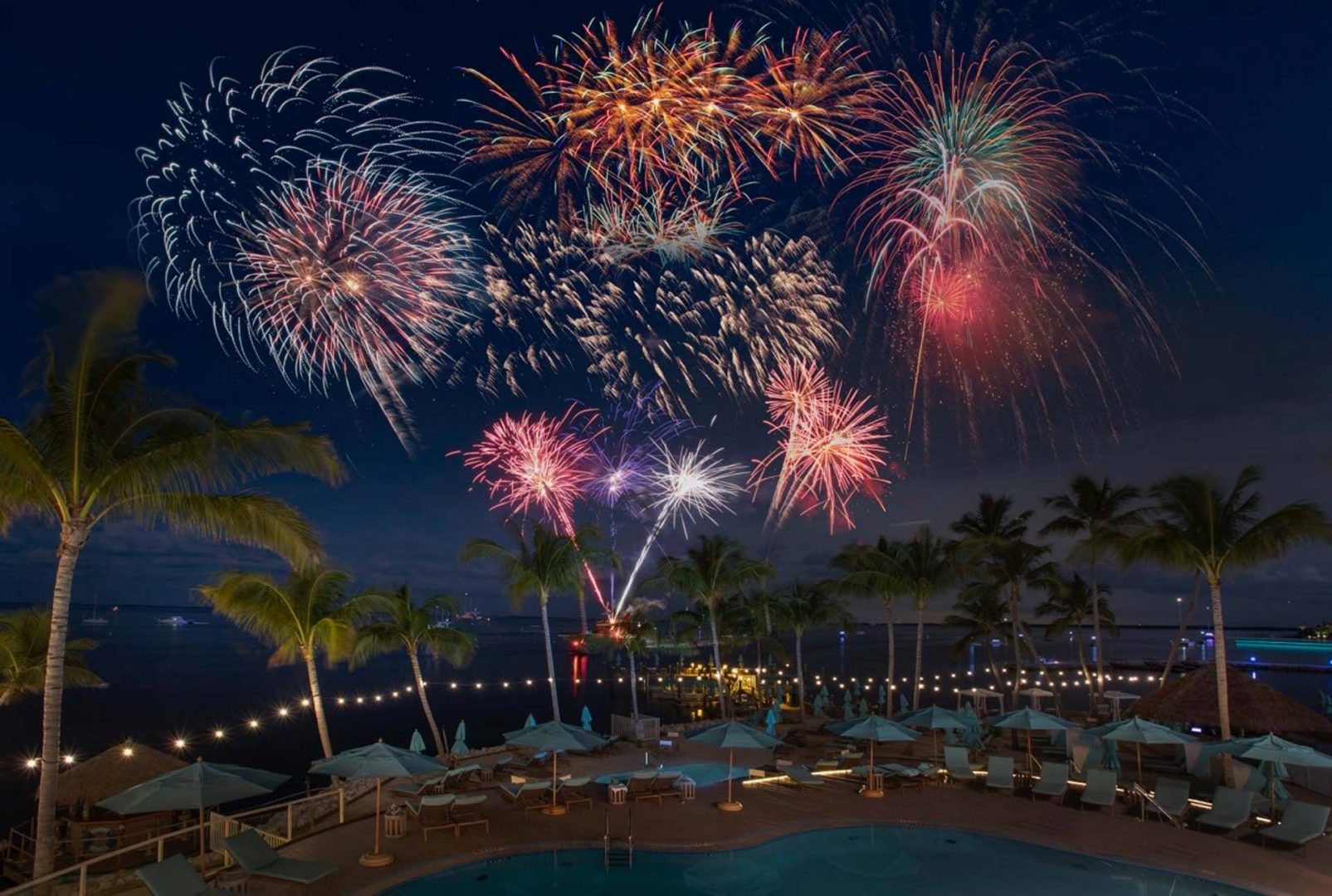 an outdoor swimming pool at night with fireworks over the water