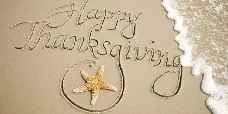 Happy Thanksgiving message handwritten outdoors in smooth brown sand with starfish and frothy white wave