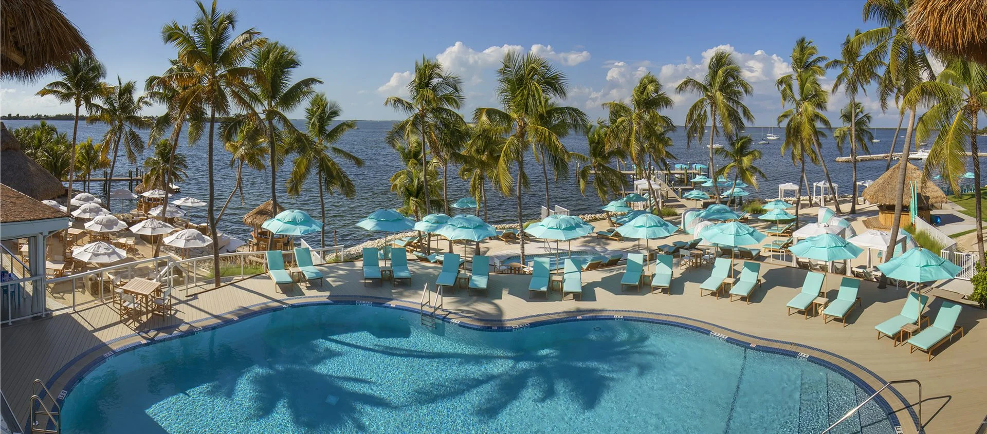 a large pool surrounded by palm trees, umbrellas, and the ocean at Bungalows Key Largo
