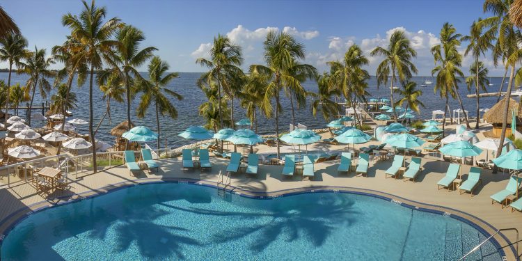 Sunset Pool DeckPano a large pool surrounded by palm trees, umbrellas, and the ocean at Bungalows Key Largo