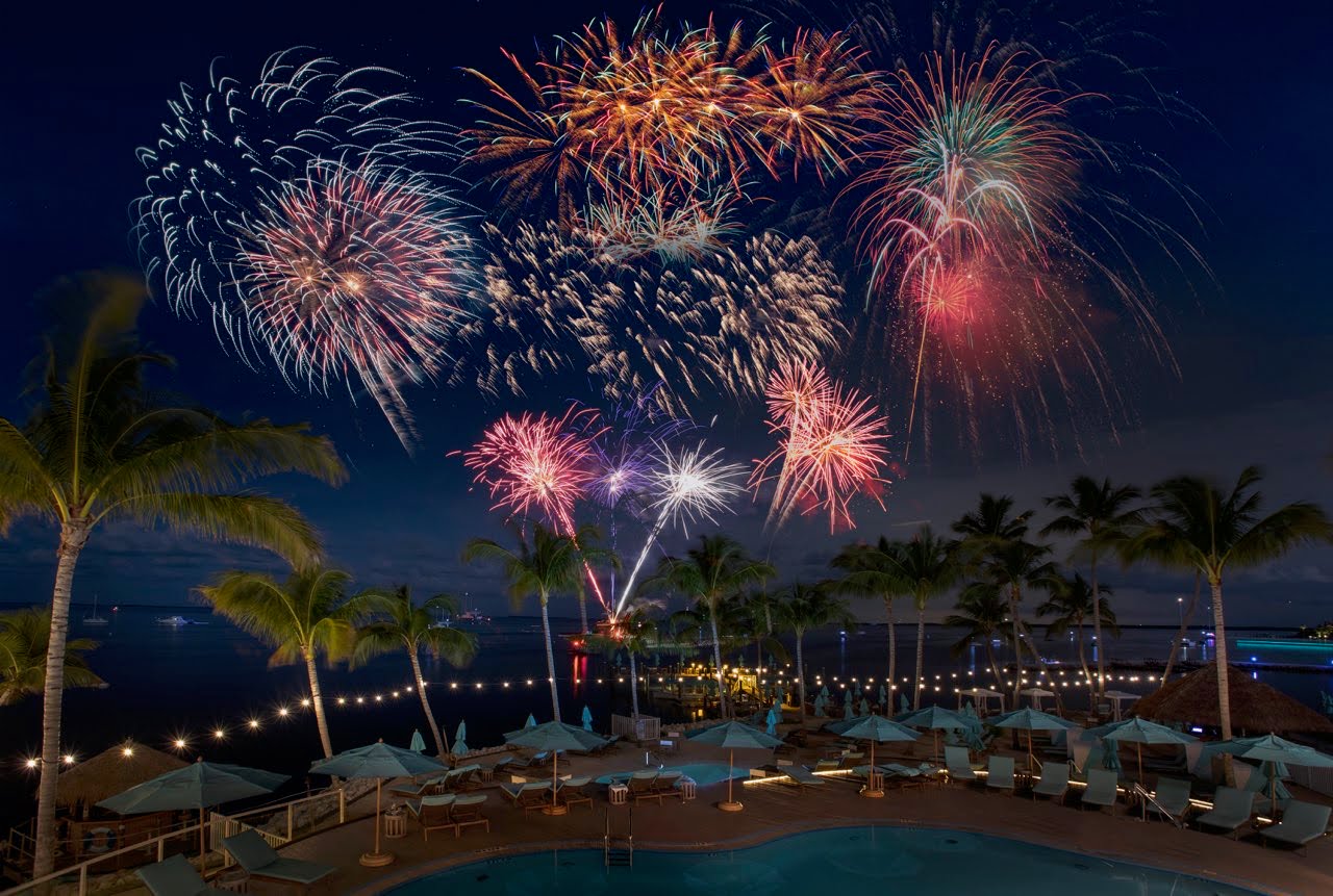 an outdoor swimming pool at night with fireworks over the water